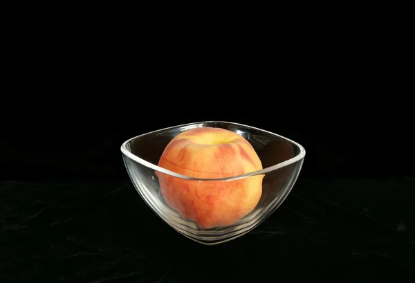 Big ripe peach in a vase of transparent glass, on black background — Stock Photo, Image