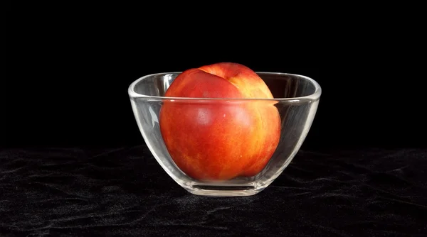 Grande nectarina madura em um vaso de vidro, em fundo preto — Fotografia de Stock