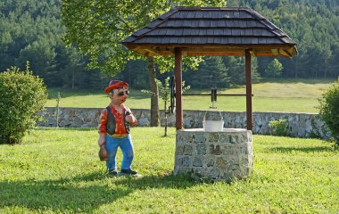 The village well for water with the comic figure of the peasant on the green grass clipart