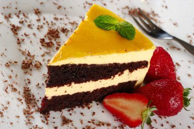 A piece of lucuma (South American fruit) cake garnished with mint leaf, chocolate shavings and strawberries (Selective Focus) clipart