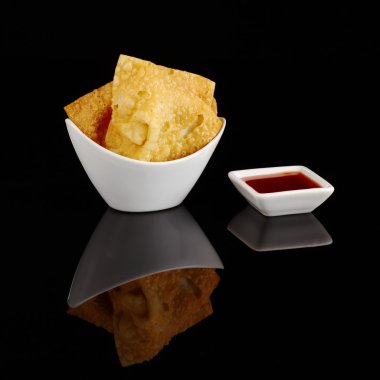 Chinese fried wantan chips in a white bowl with a sweet red sauce on black clipart