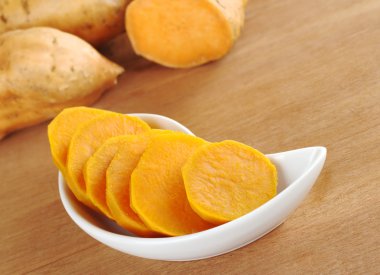 Cooked sweet potato (lat. Ipomoea batatas) cut in slices in white bowl on wooden surface with sweet potatoes in the background (Selective Focus) clipart