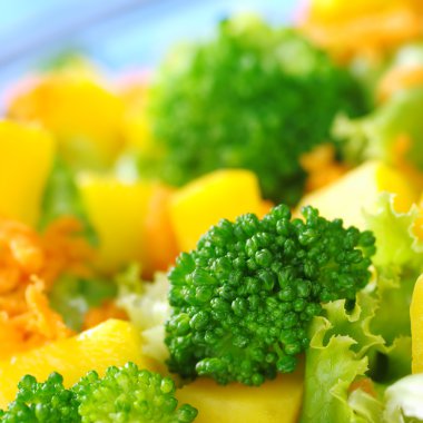 Broccoli on fresh salad (broccoli, mango, carrot, lettuce) in a bowl with blue background (Very Shallow Depth of Field, Focus on the front of the broccoli) clipart