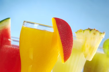 Mango, melon, pineapple and kiwi smoothies garnished with the corresponding fruit on the rim on blue background (Selective Focus, Focus on the mango smoothie in clipart