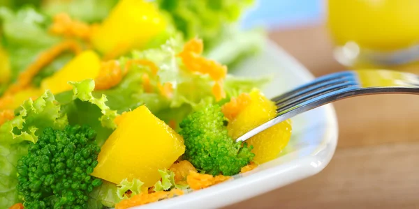 新鲜和轻西兰花 胡萝卜沙拉在白板上与一块叉上芒果和一杯橙汁敷料在后面 — 图库照片