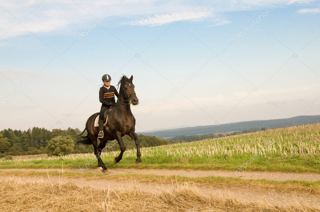 Equestrienne rides at a gallop on a brown horse.
