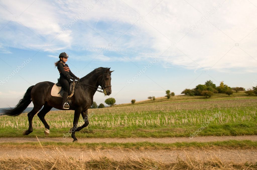Equestrienne rides at a gallop on the field road.