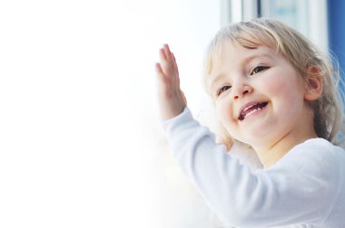 Cheerful little girl sits at window portrait clipart