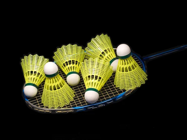 Raquette de badminton avec six navettes jaunes isolées sur fond noir — Photo