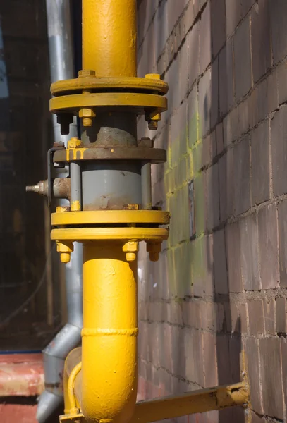 Жовта газова труба з краном на коричневій стіні — стокове фото