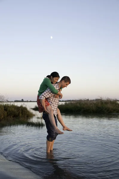Meisje op jongens terug permanent in het water — Stockfoto