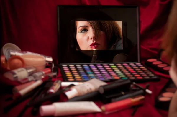 Woman in mirror applying makeup. Red background.