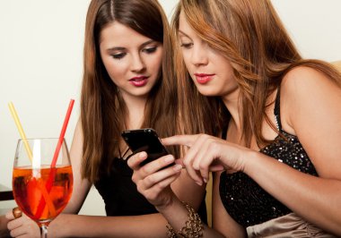 Girls showing cool stuff on a mobile phone to her friend clipart