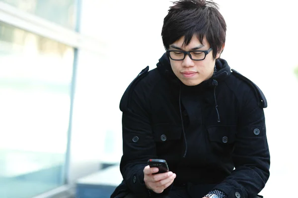 Случайный азиатский мужчина смс на мобильный телефон — стоковое фото