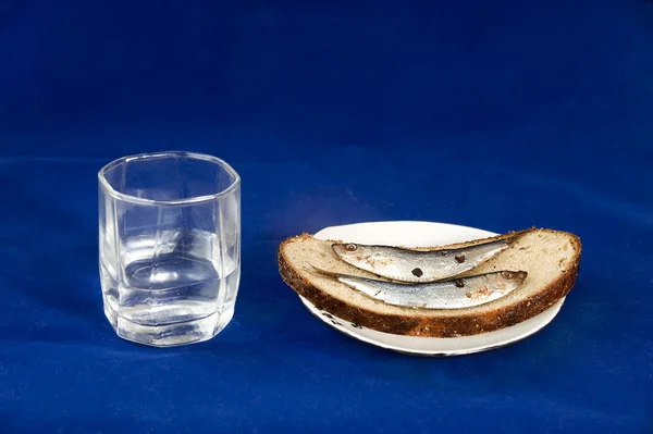 stock image Glass of vodka and sandwich with a sprat on a dark blue background