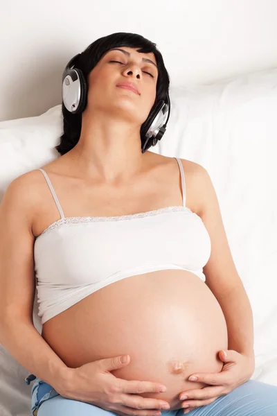 Беременная женщина сидит на диване и слушает музыку — стоковое фото