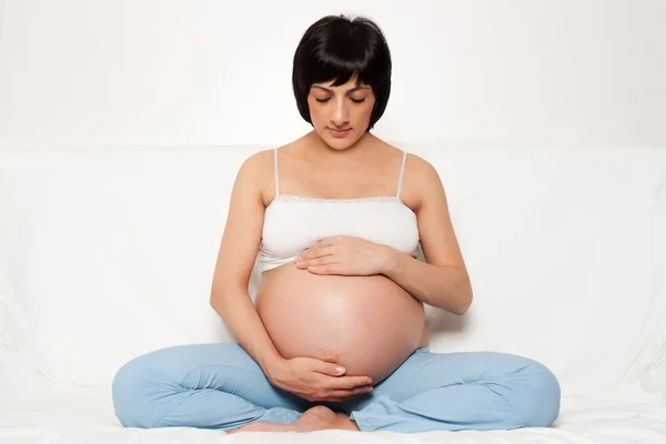 Έγκυος γυναίκα που κάθεται σε έναν καναπέ Εικόνα Αρχείου