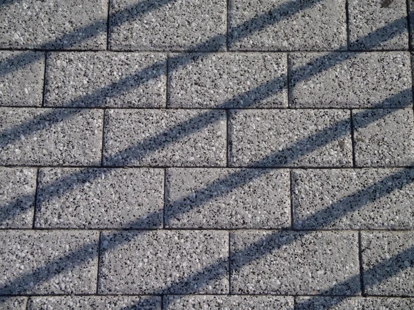 Caminho de tijolo cinza com linhas de sombra cruzando sobre ele — Fotografia de Stock