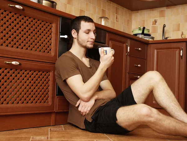 Guy on the floor in the kitchen with cup of tea — Stock Photo, Image