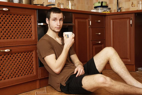 Um tipo no chão da cozinha com uma chávena de chá. — Fotografia de Stock