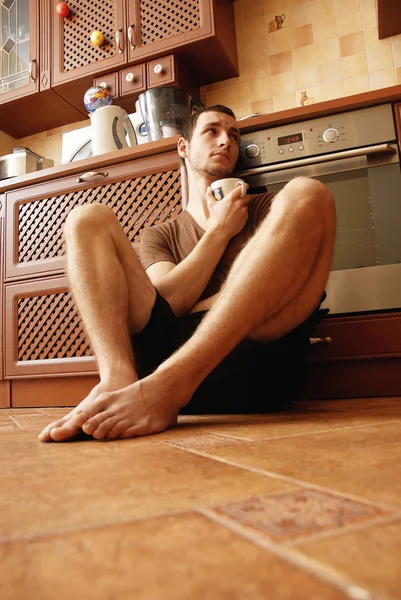Um tipo no chão da cozinha com uma chávena de chá. — Fotografia de Stock