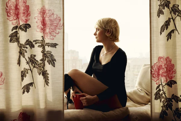 Portrait of charming girl sitting on windowsill and looking thro — Stock Photo, Image