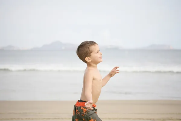 Młody chłopak gra na plaży i fale — Zdjęcie stockowe