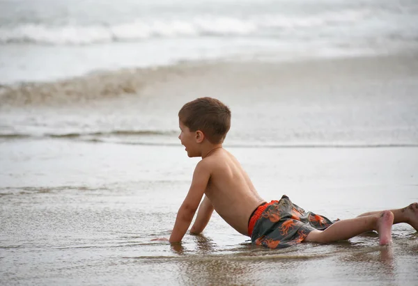 Mladý chlapec hraje na pláži a vlny — Stock fotografie