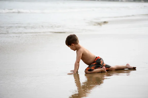 Mladý chlapec hraje na pláži a vlny — Stock fotografie