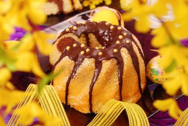 Marble ring cake poured with chocolate on easter table in purple color and yellow forsythia flowers around clipart