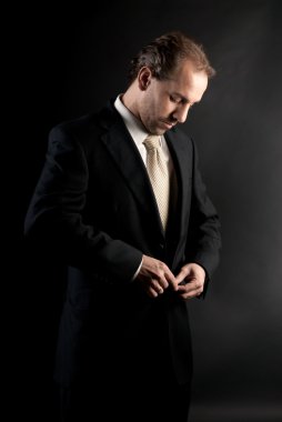Businessman buttoning jacket, getting dressed, on dark background clipart