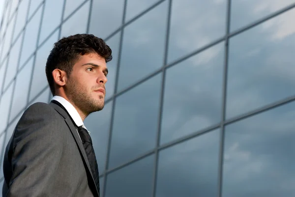 Joven hombre de negocios mirando hacia un buen futuro en el fondo del edificio moderno — Foto de Stock