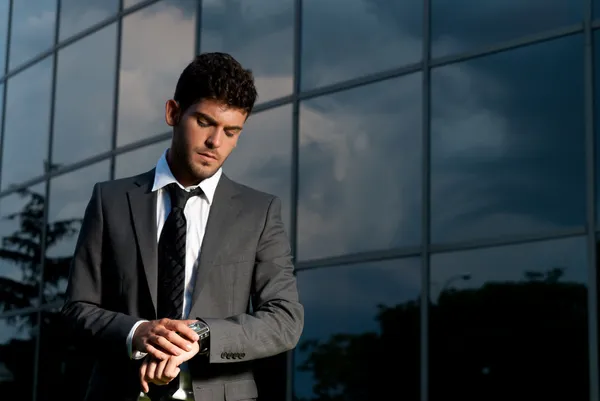 Giovane uomo d'affari in cerca di orologio di notte su sfondo edificio moderno — Foto Stock