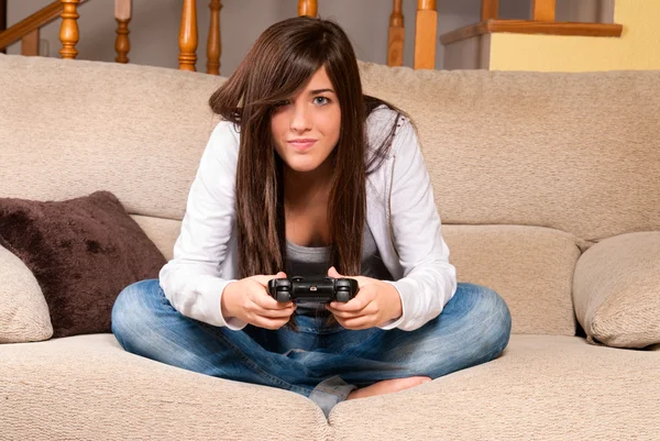 Joven hembra concentrada jugando videojuegos en el sofá en casa Imágenes de stock libres de derechos