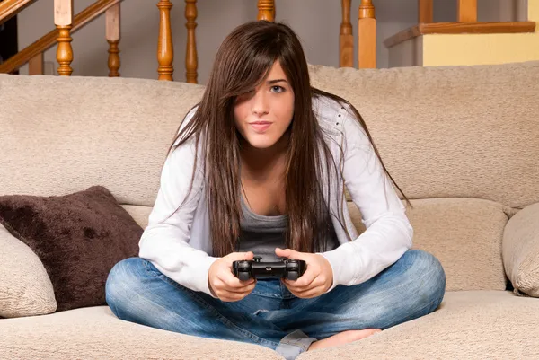 Молодая женщина концентрируется, играя в видеоигры на диване дома Стоковая Картинка