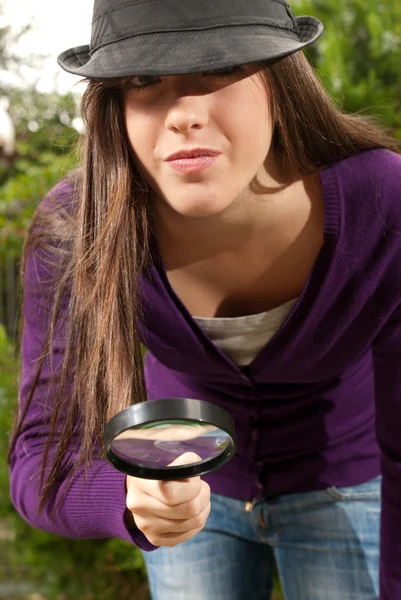 Young woman with magnifier glass and hat looking for something on outdoors — Stock Photo, Image