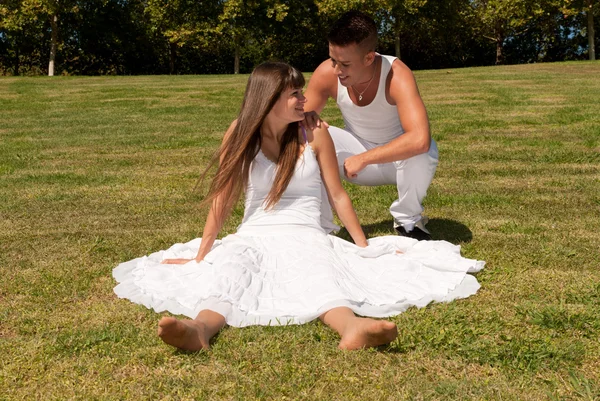 Jeune couple heureux assis sur herbe vêtements blancs, relation amoureuse — Photo