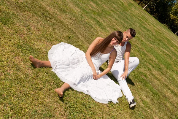 Junges Paar glücklich sitzt auf Gras weiße Kleidung, Liebesbeziehung — Stockfoto