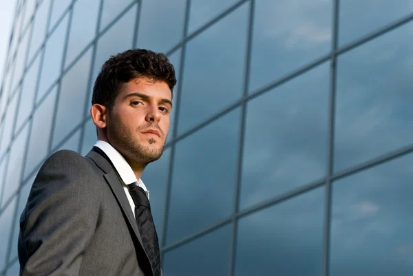 Young businessman looking to camera on modern building background — Stock Photo, Image
