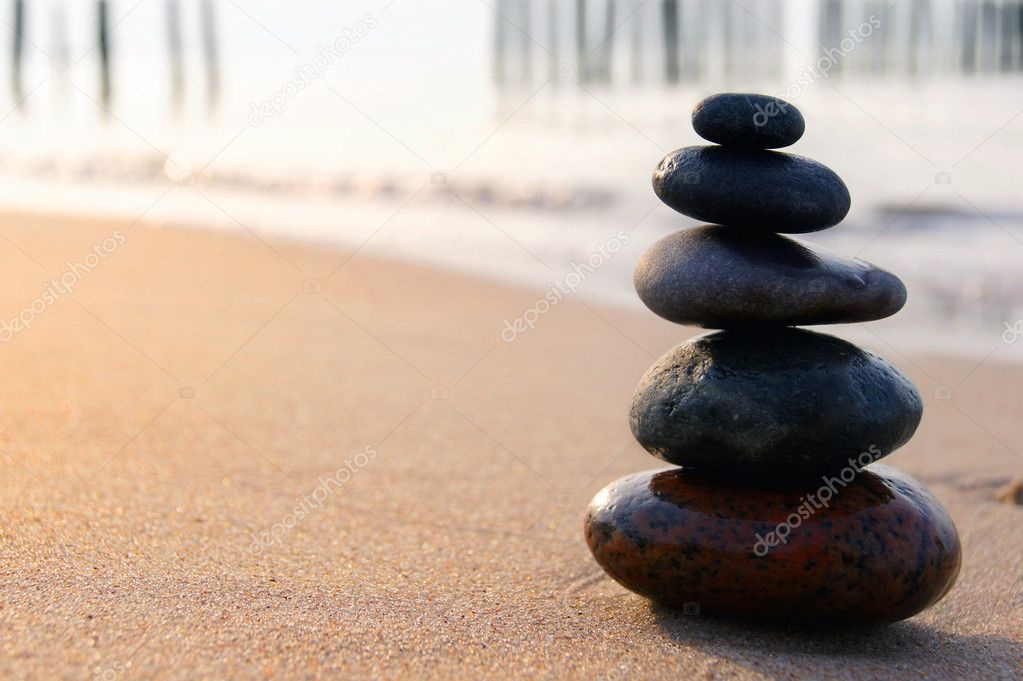 Zen stones balancing on the sandy seashore at sunset