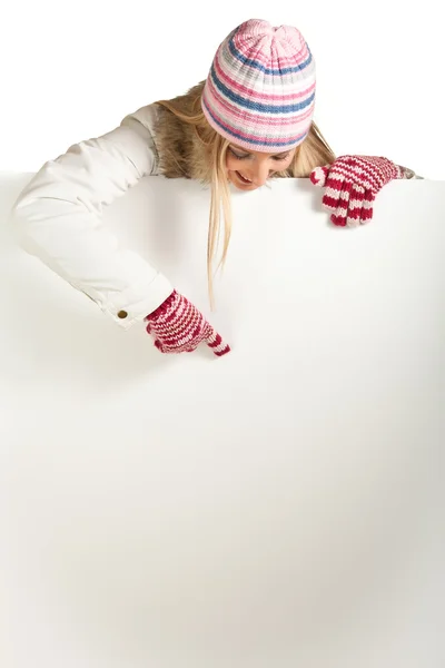 Frau mit bunter Mütze und Handschuhen guckt hinter Whiteboard isoliert auf — Stockfoto