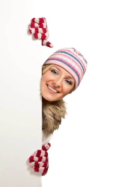 Woman in colorful hat and gloves peeping from behind whiteboard isolated on — Stock Photo, Image
