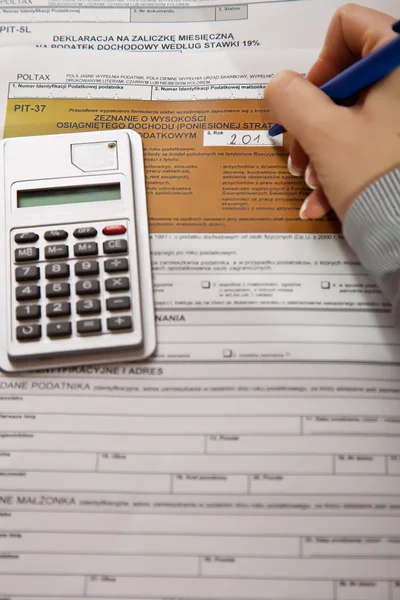 Kvinna hand fylla inkomstskatt former med miniräknare — Stockfoto