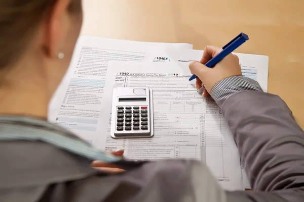 Рука жінки заповнює форми податку на прибуток калькулятором — стокове фото