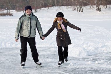 A young couple enjoys a leisurely skate in winter. clipart