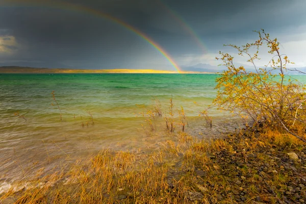 Rainbow and dark clouds over large lake — Stock Photo, Image