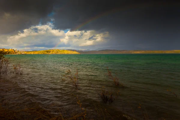 Rainbow and dark clouds over large lake — Stock Photo, Image