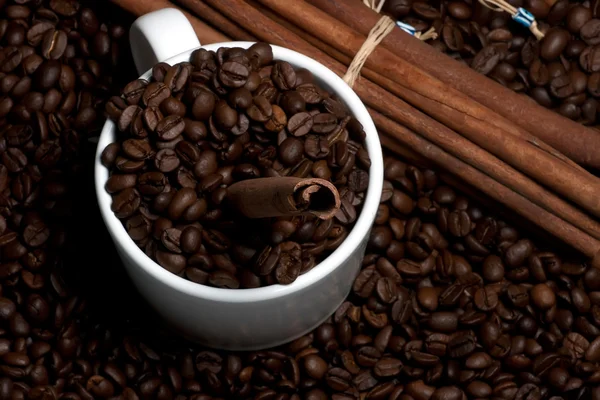 White mug with cinnamon sticks on coffee beans — Stock Photo, Image