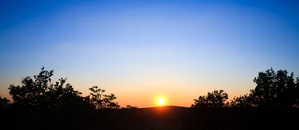 Trauriger Sonnenuntergang mit Sonne und Silhouette von Bäumen und Bergen — Stockfoto