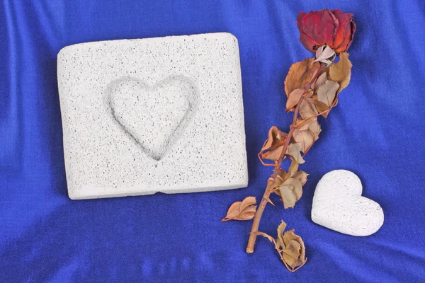 Встановлення кам'яних сердець і сушеної троянди на синьому атласі Стокове Зображення